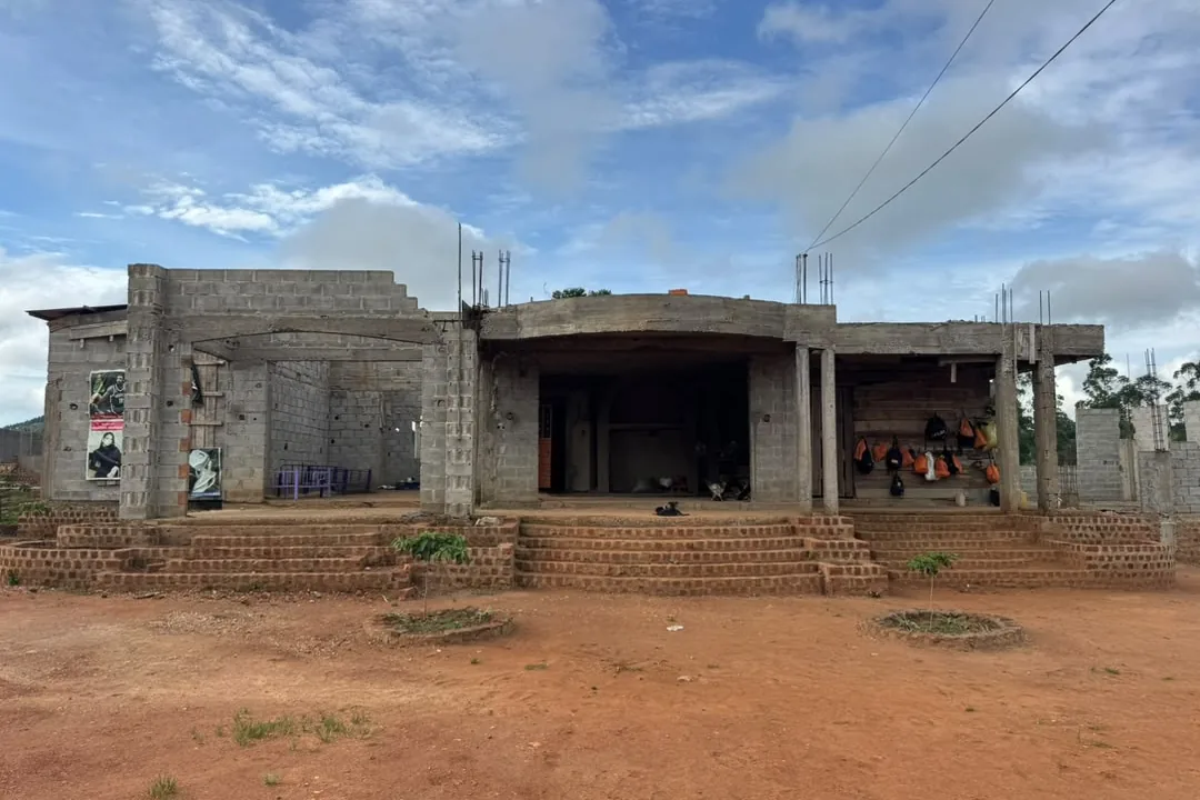 Facade of the house under construction: exposed concrete blocks, a slab and brick steps.