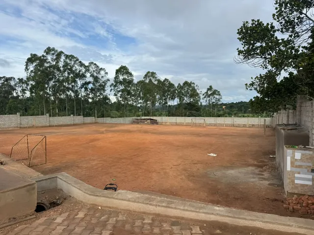 Red earth pitch with two goals, surrounded by a block wall and tall trees.