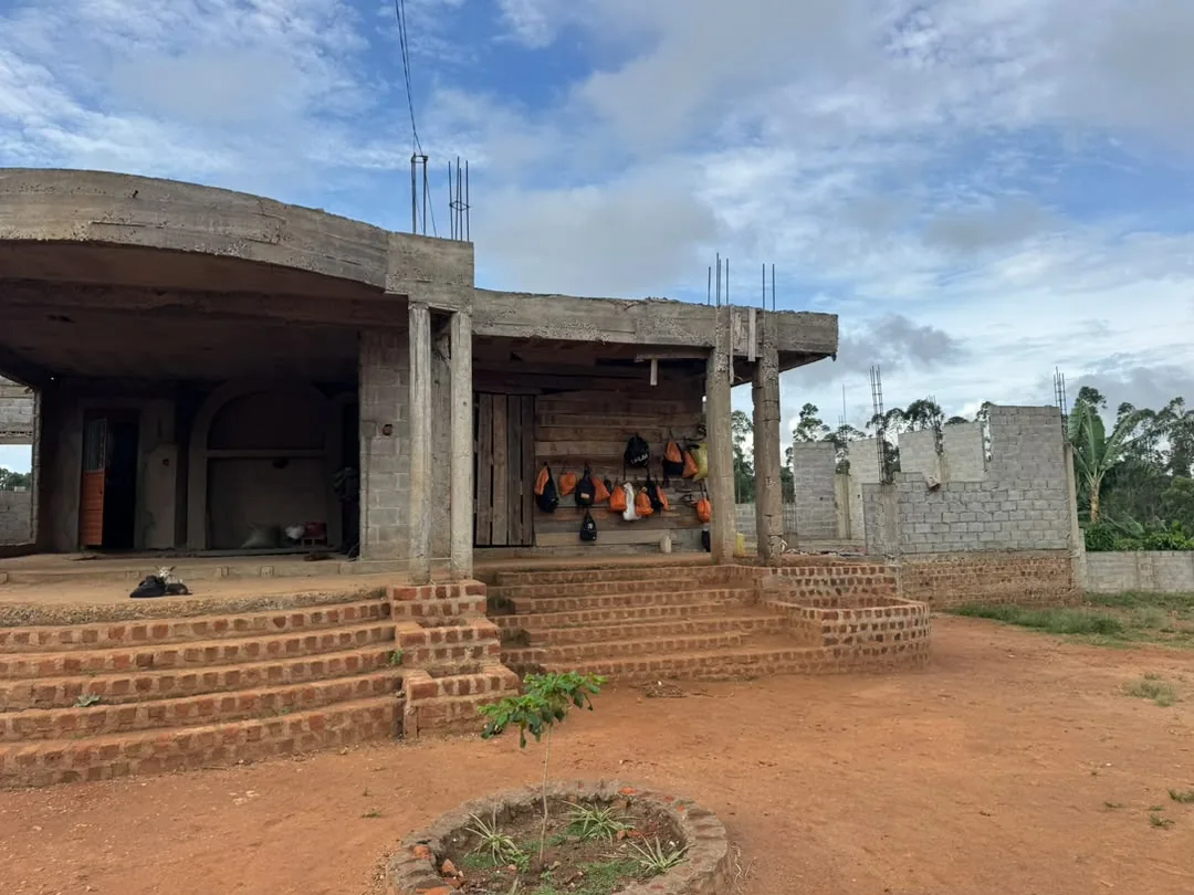 Veranda of the house under construction: concrete pillars, curved brick steps and colorful backpacks hanging on the wall.
